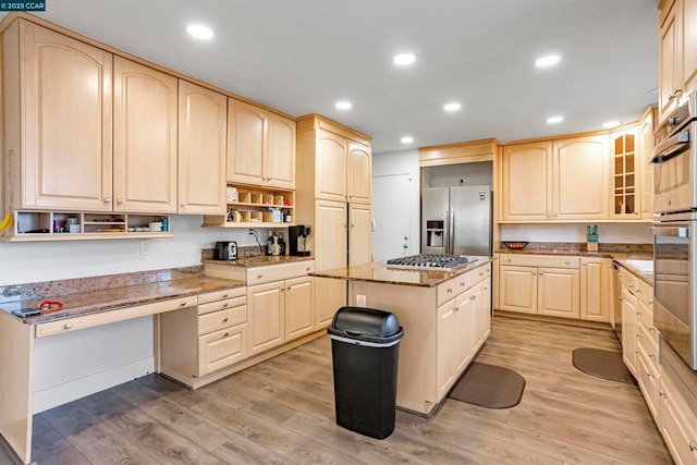 kitchen featuring light wood-type flooring, a kitchen island, light brown cabinetry, and appliances with stainless steel finishes