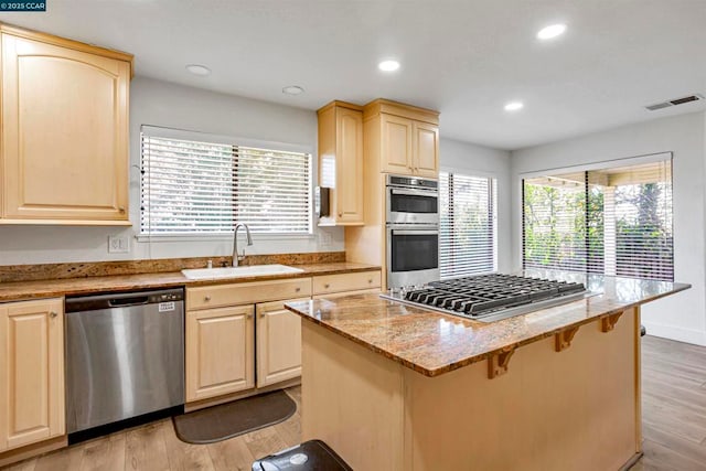 kitchen with light hardwood / wood-style floors, sink, appliances with stainless steel finishes, and a breakfast bar area