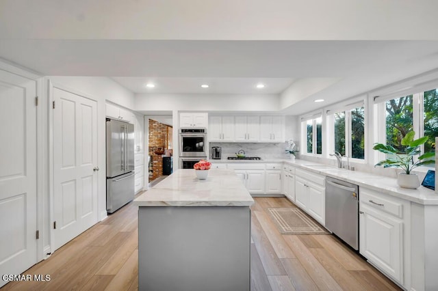 kitchen with sink, a center island, appliances with stainless steel finishes, light stone countertops, and white cabinets