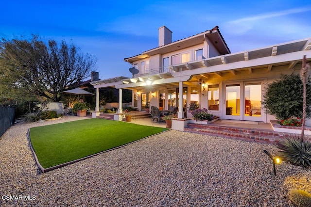 back house at dusk with a pergola, a patio, and a lawn