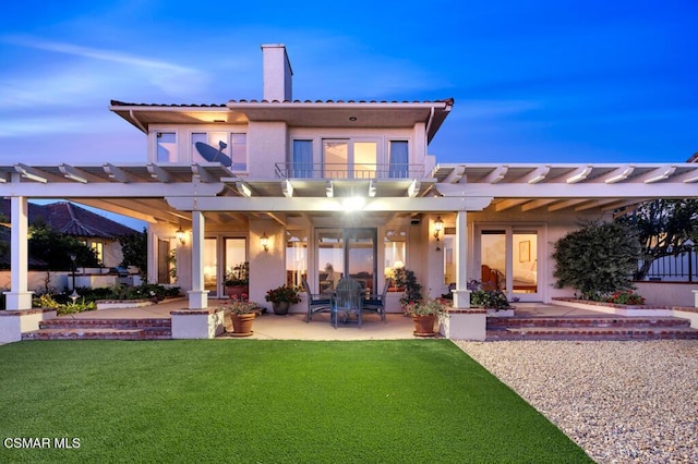 back house at dusk featuring a balcony, a yard, a pergola, and a patio