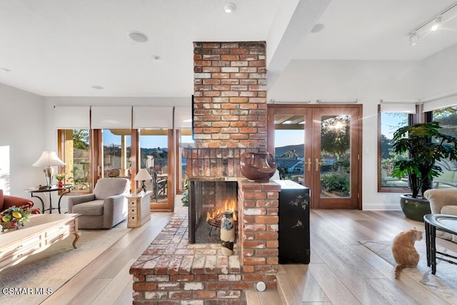 living room with a fireplace, track lighting, french doors, and light wood-type flooring