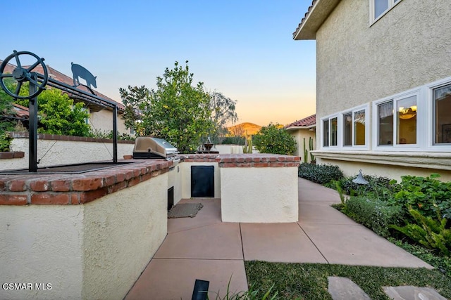 patio terrace at dusk with an outdoor kitchen and area for grilling