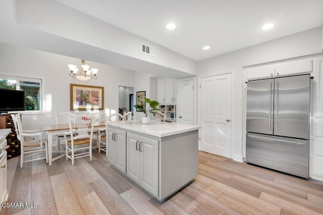 kitchen featuring hanging light fixtures, light wood-type flooring, white cabinets, and built in refrigerator