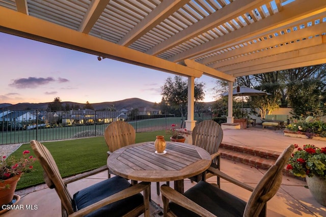 patio terrace at dusk with a mountain view, a pergola, and a yard