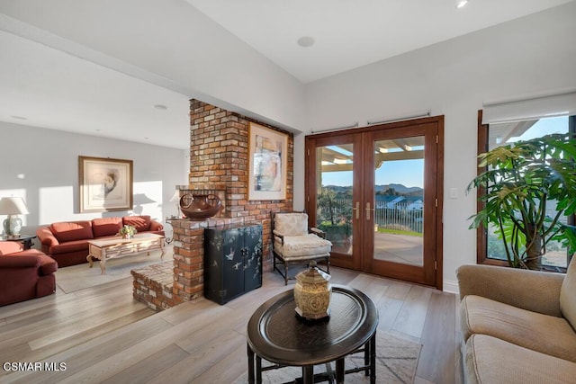 living room with french doors, a water view, a brick fireplace, and light hardwood / wood-style flooring