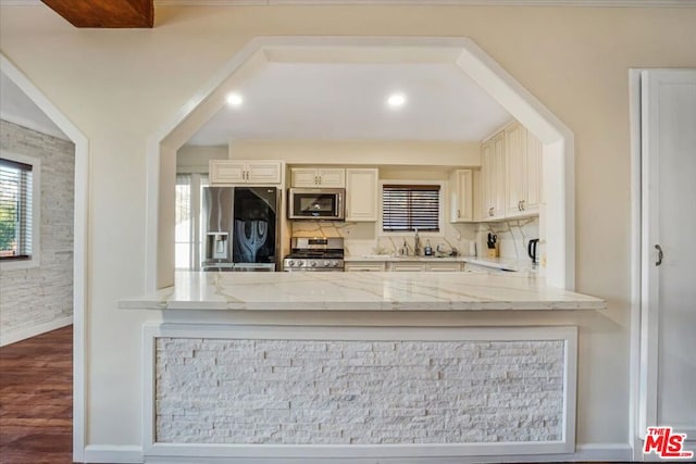 kitchen with light stone counters, appliances with stainless steel finishes, cream cabinets, and a healthy amount of sunlight