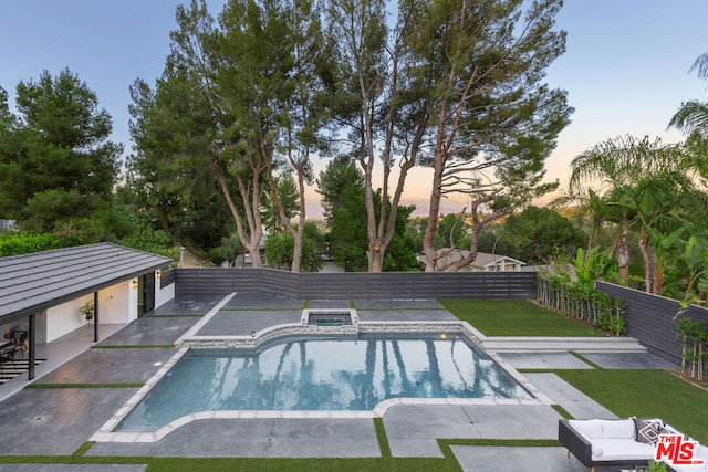 pool at dusk with an in ground hot tub, a patio, and a yard