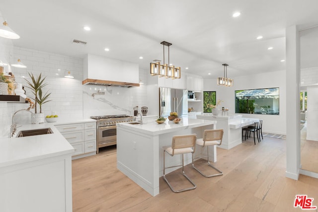 kitchen with custom exhaust hood, appliances with stainless steel finishes, white cabinetry, a kitchen island with sink, and a breakfast bar area