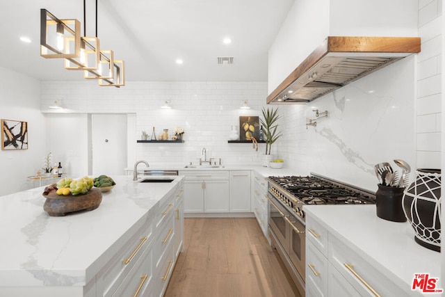 kitchen with premium range hood, hanging light fixtures, white cabinets, sink, and double oven range