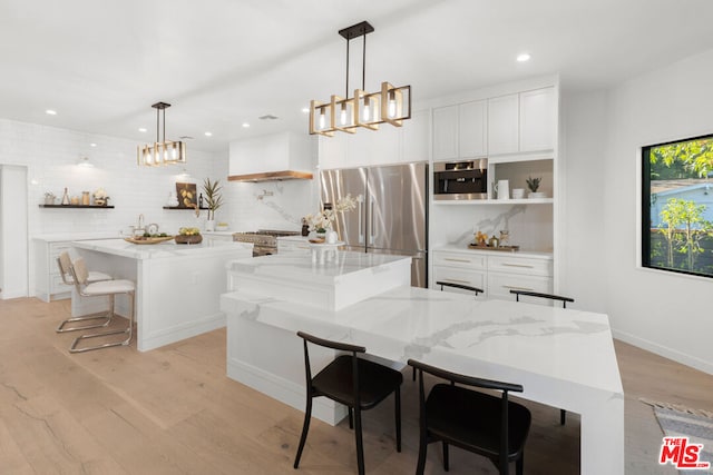 kitchen featuring white cabinets, appliances with stainless steel finishes, decorative light fixtures, a large island, and light stone counters