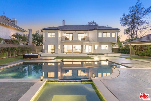 back house at dusk with a swimming pool with hot tub, a balcony, and a patio