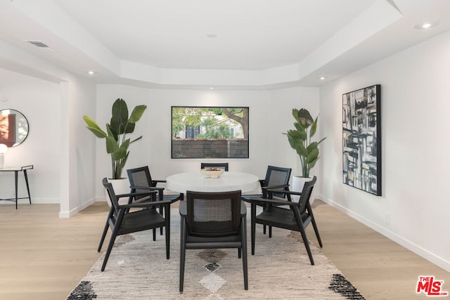 dining area with light hardwood / wood-style floors and a tray ceiling