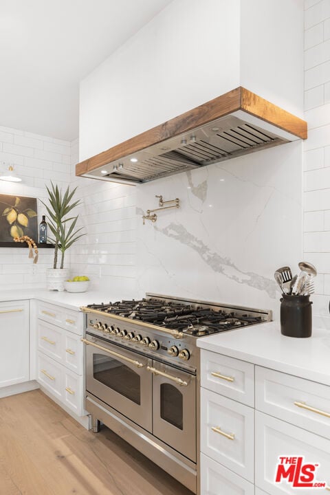 kitchen featuring custom exhaust hood, white cabinetry, tasteful backsplash, double oven range, and light wood-type flooring