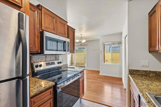 kitchen with light wood-type flooring, stainless steel appliances, dark stone countertops, and an inviting chandelier