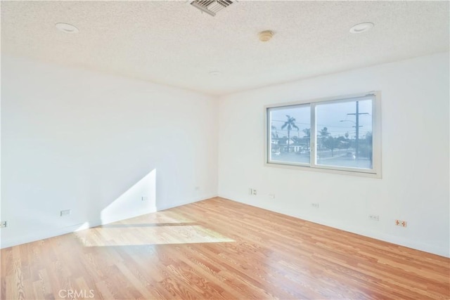 empty room with visible vents, a textured ceiling, and wood finished floors