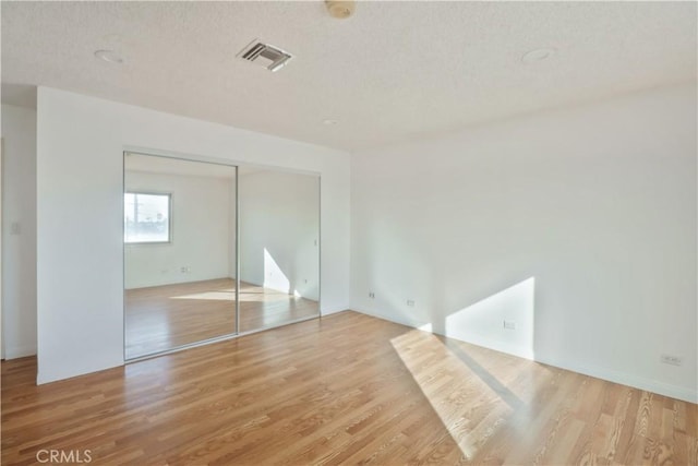 unfurnished bedroom with light wood-style floors, a textured ceiling, visible vents, and a closet