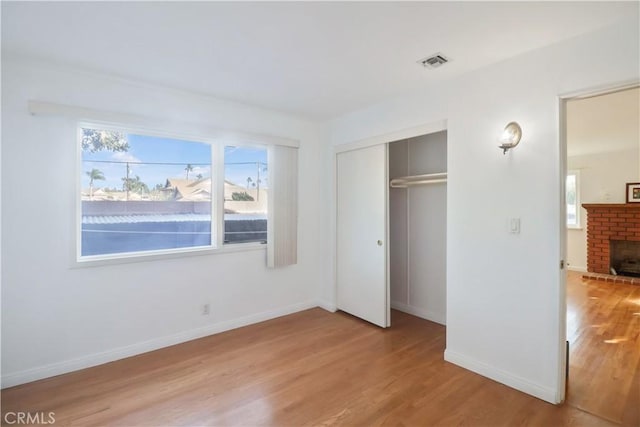 unfurnished bedroom featuring visible vents, a fireplace, light wood-style flooring, and baseboards