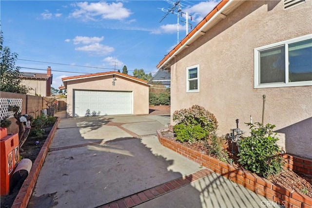 view of side of property featuring an outbuilding, a detached garage, fence, and stucco siding