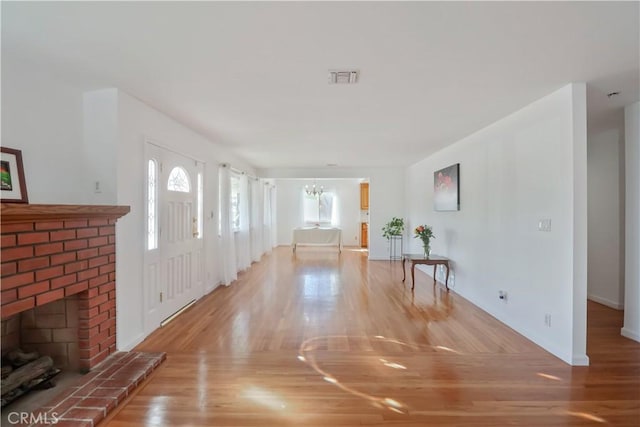 entryway with a chandelier, a brick fireplace, visible vents, and wood finished floors