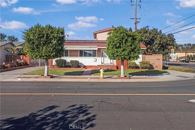 obstructed view of property with driveway, a tile roof, solar panels, and a front yard