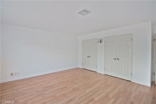 unfurnished bedroom with baseboards, light wood finished floors, visible vents, and multiple closets