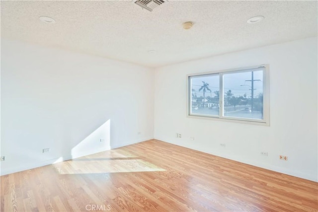 empty room with visible vents, a textured ceiling, and wood finished floors