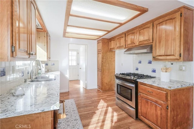 kitchen with light hardwood / wood-style floors, sink, stainless steel gas stove, backsplash, and light stone counters