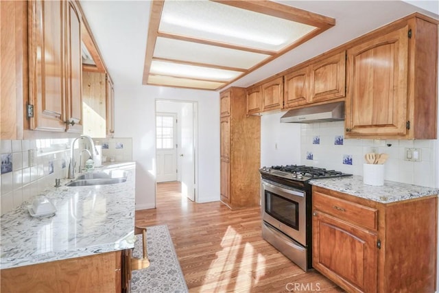 kitchen featuring under cabinet range hood, a sink, light wood finished floors, tasteful backsplash, and gas range