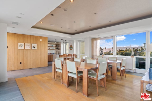 dining room featuring light wood-type flooring, a raised ceiling, and wooden walls