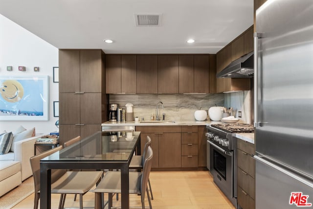 kitchen with premium appliances, sink, light wood-type flooring, range hood, and dark brown cabinetry