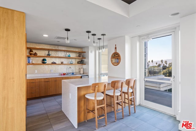 kitchen featuring a kitchen bar, decorative light fixtures, tasteful backsplash, sink, and kitchen peninsula