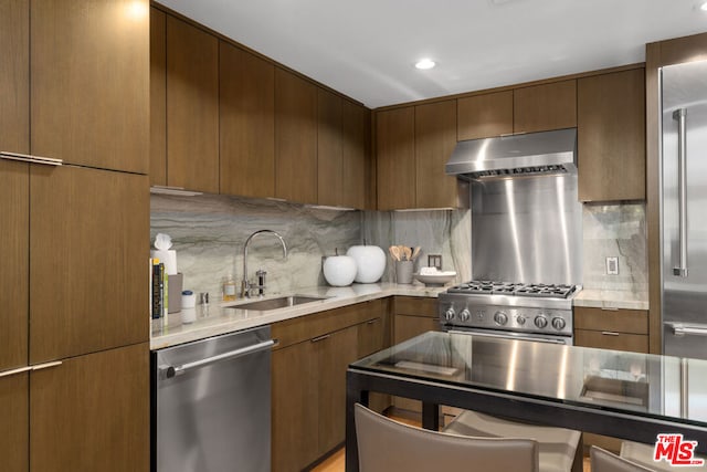 kitchen featuring light stone countertops, decorative backsplash, sink, range hood, and high quality appliances