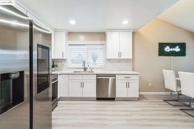 kitchen featuring sink, appliances with stainless steel finishes, white cabinets, decorative backsplash, and light wood-type flooring