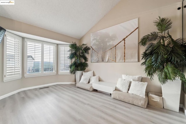 sitting room featuring lofted ceiling, light hardwood / wood-style flooring, and a textured ceiling