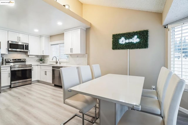 kitchen featuring sink, light wood-type flooring, appliances with stainless steel finishes, decorative backsplash, and white cabinets