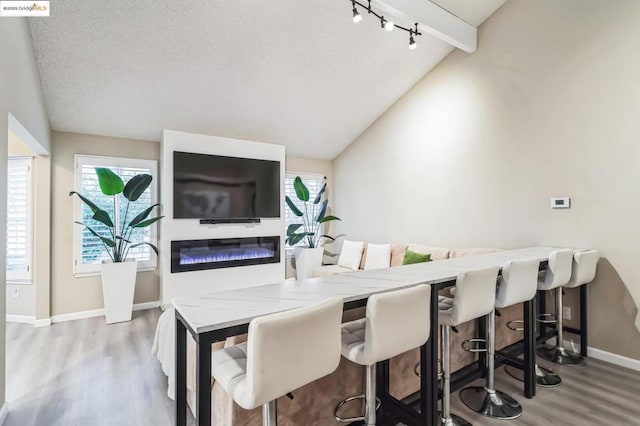 dining room featuring rail lighting, hardwood / wood-style floors, a textured ceiling, and vaulted ceiling with beams