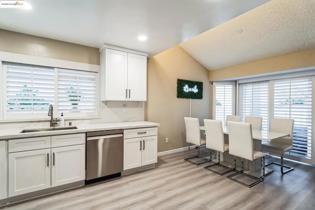 kitchen featuring lofted ceiling, sink, white cabinets, stainless steel dishwasher, and light hardwood / wood-style flooring