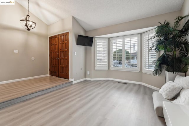 entryway featuring vaulted ceiling, wood-type flooring, a textured ceiling, and a chandelier