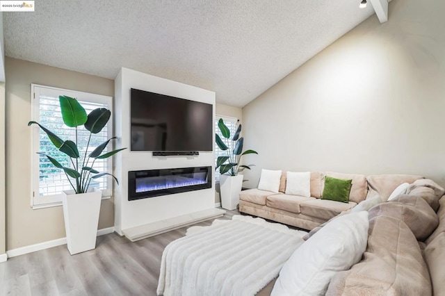 living room featuring a healthy amount of sunlight, lofted ceiling with beams, a textured ceiling, and light wood-type flooring