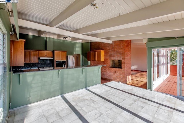 kitchen with kitchen peninsula, backsplash, oven, beamed ceiling, and stainless steel refrigerator