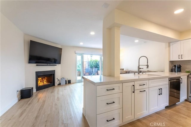 kitchen with kitchen peninsula, white cabinets, light hardwood / wood-style flooring, and sink