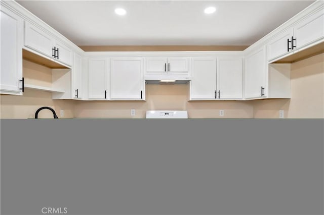 kitchen with under cabinet range hood, recessed lighting, white cabinets, and stove