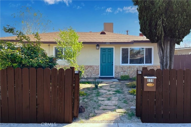view of front of property with stone siding, fence, stucco siding, and a gate