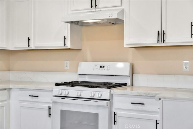 kitchen with white gas stove, under cabinet range hood, white cabinets, and light stone counters