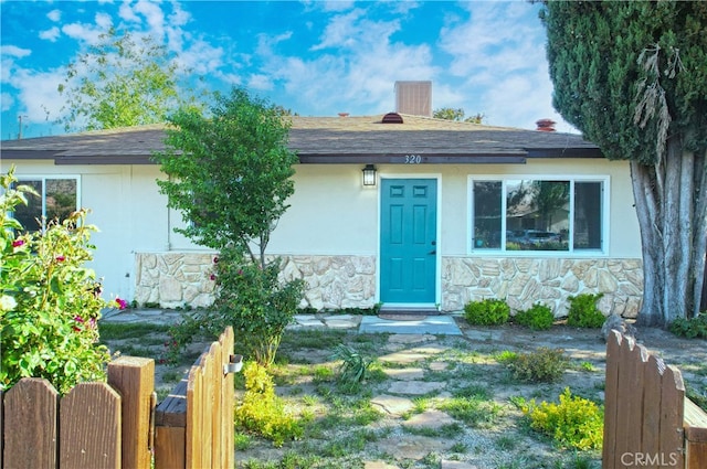 view of front facade featuring stone siding, stucco siding, fence, and a gate