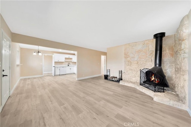 unfurnished living room featuring light wood finished floors, baseboards, a wood stove, and a sink