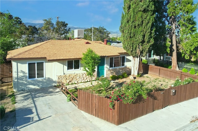 ranch-style home with roof with shingles, fence, cooling unit, stone siding, and a mountain view