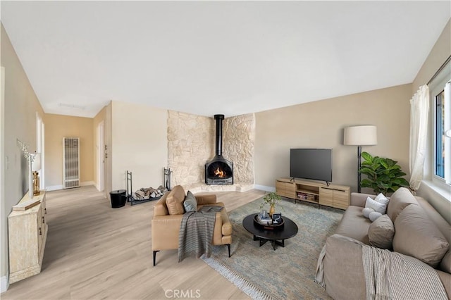 living area featuring light wood-type flooring, a heating unit, baseboards, and a wood stove