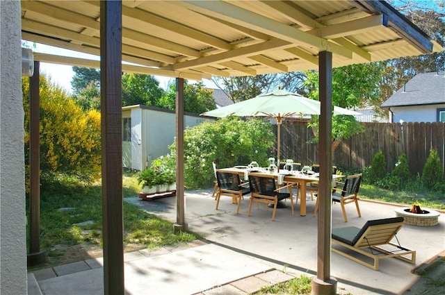 view of patio with an outdoor fire pit, outdoor dining area, fence, an outdoor structure, and a storage unit